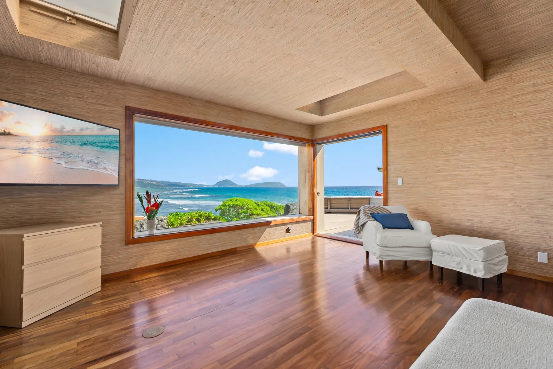 A bright living room with large windows overlooking the ocean and seating by the open doorway.