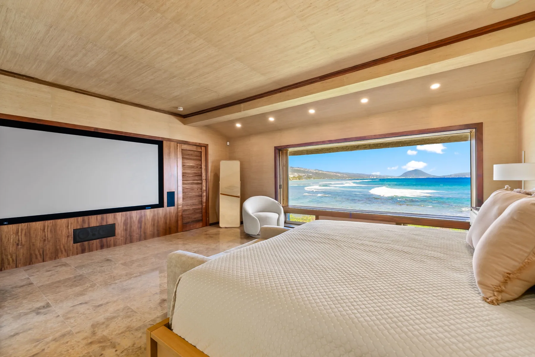 A bedroom with a large bed, a wall-mounted screen, and a wide ocean view.