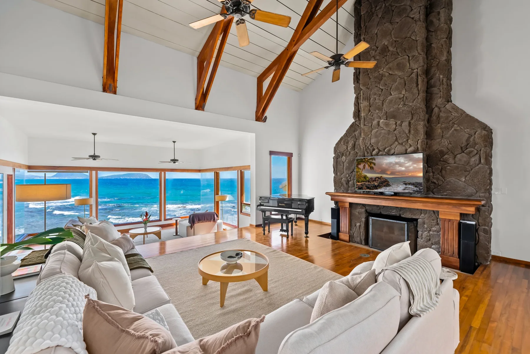 A bright living room with seating, a large stone fireplace, and ocean views through wide windows.