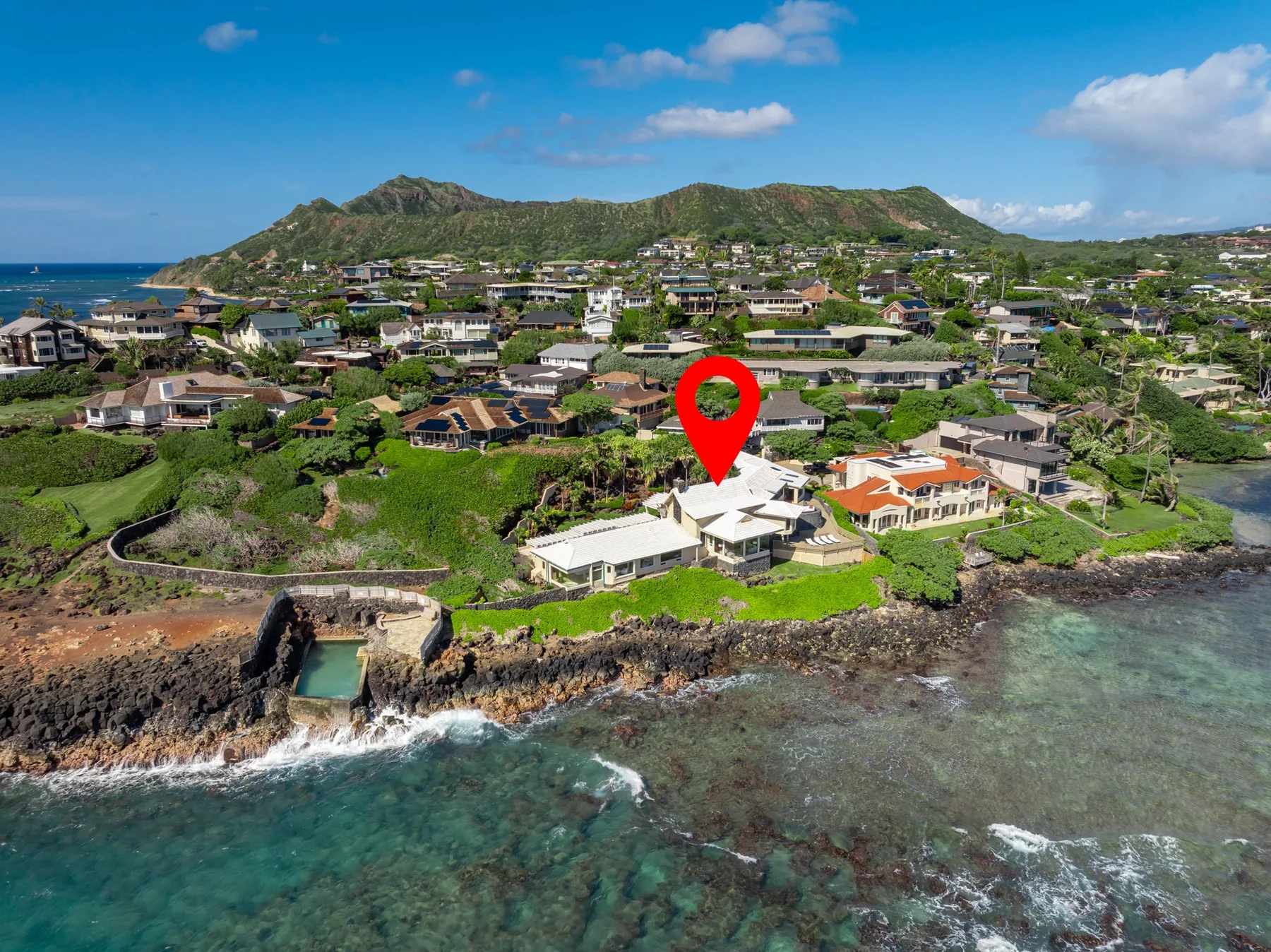 Aerial coastal view of homes along a rocky shore, with green hills in the background.