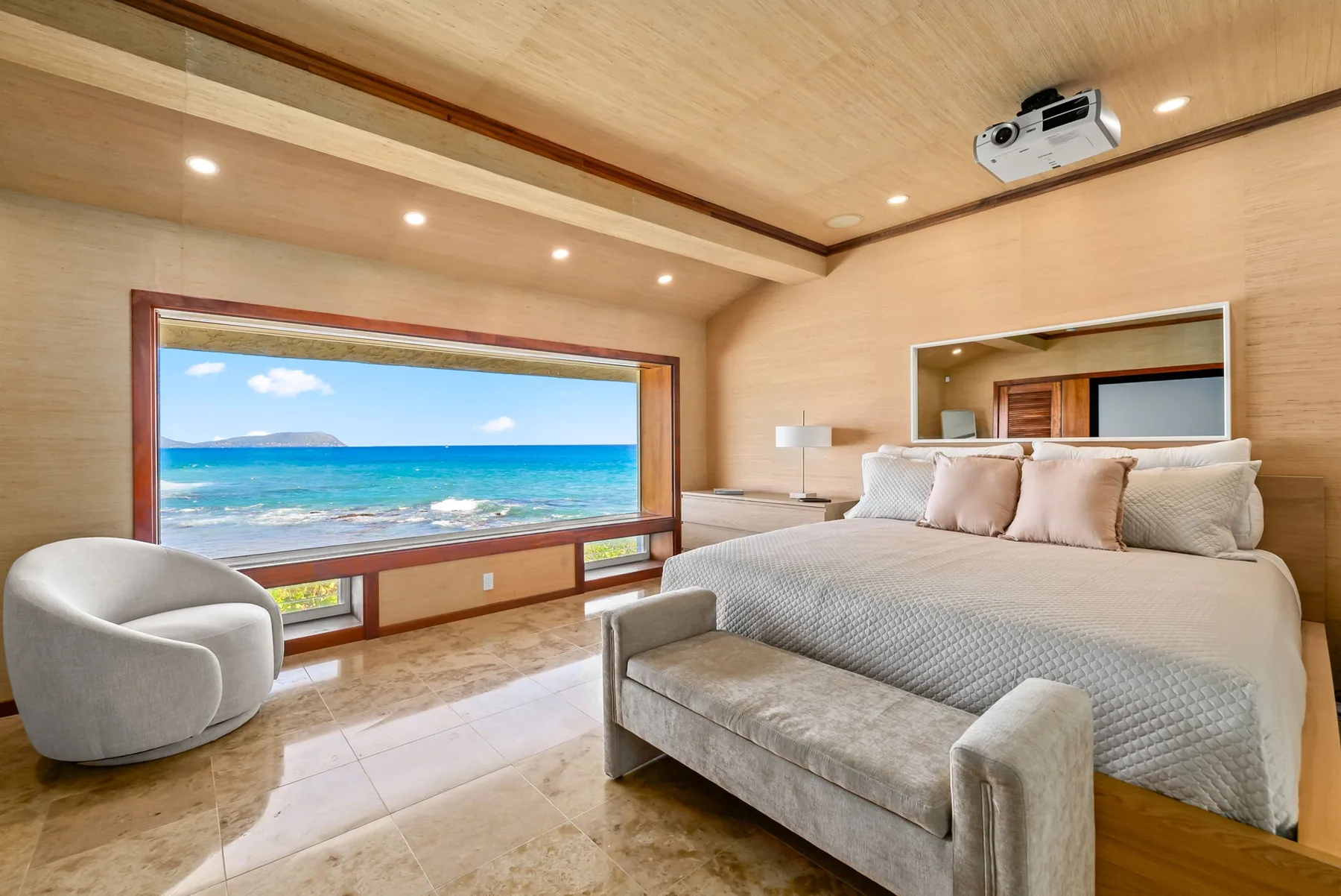 A bedroom with a large bed beside a wide window overlooking the ocean.
