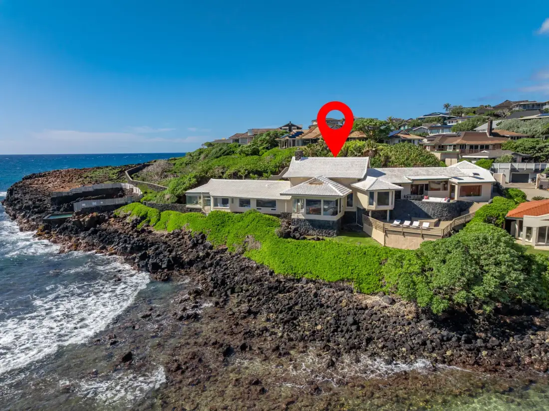 A coastal house sits above a rocky shoreline, with green vegetation around it.