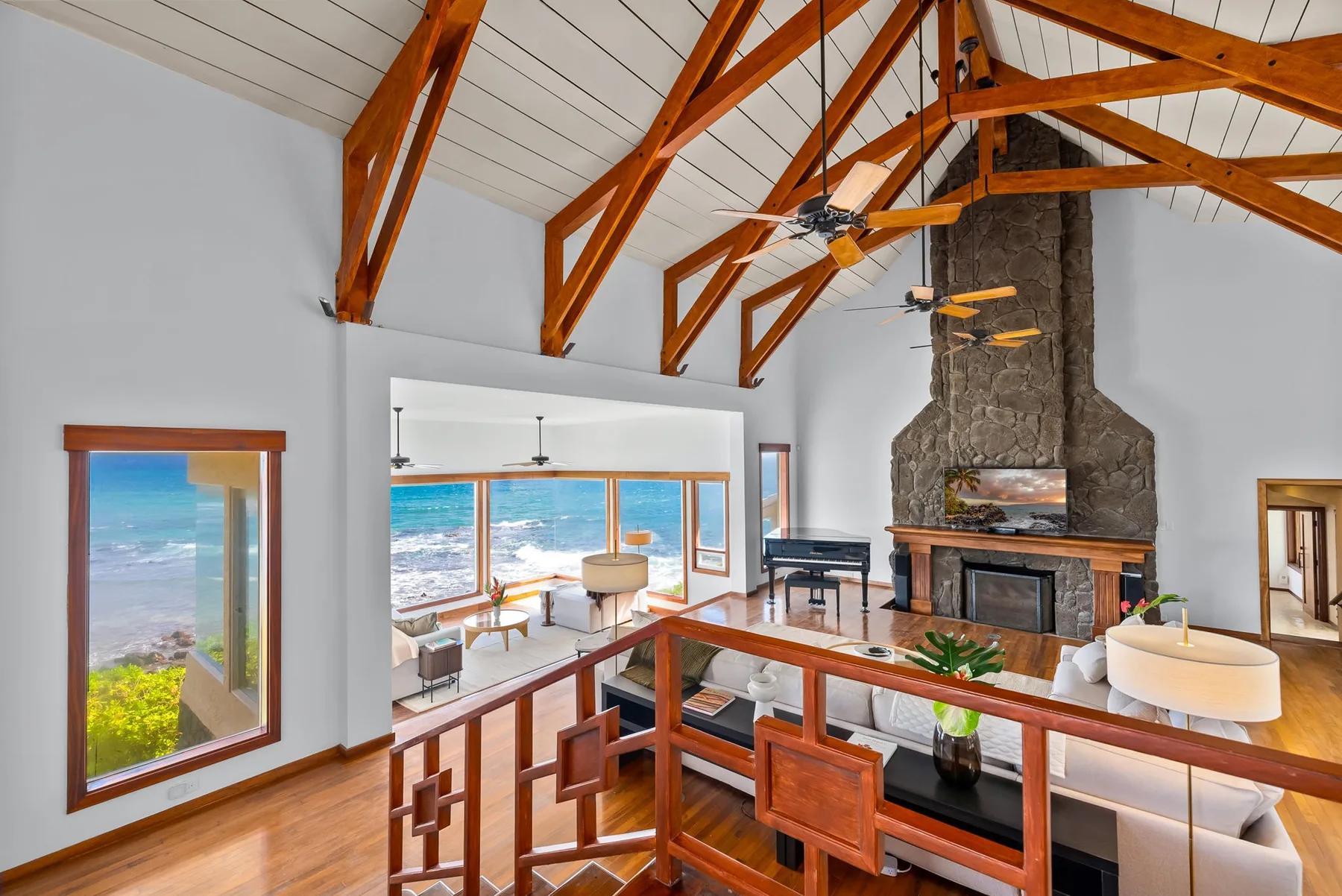 A bright living room with exposed wooden ceiling beams and a large stone fireplace.