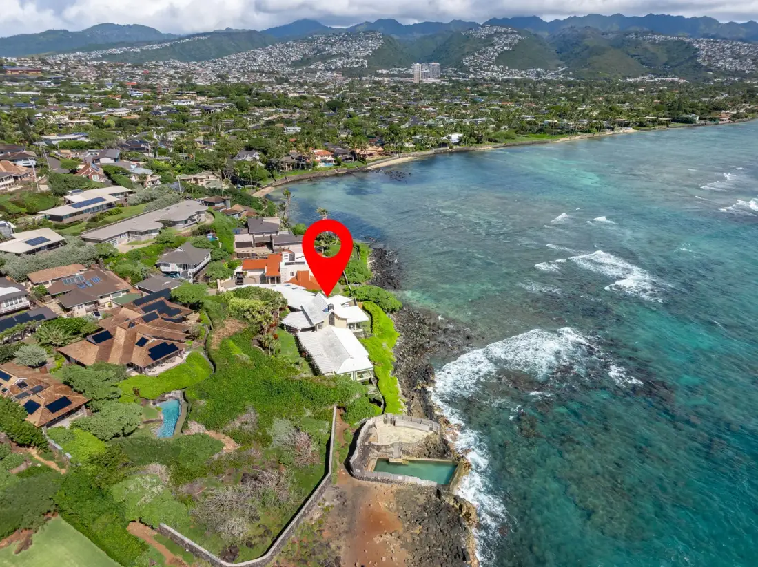 Aerial view of a coastal neighborhood beside a turquoise bay and green hills.