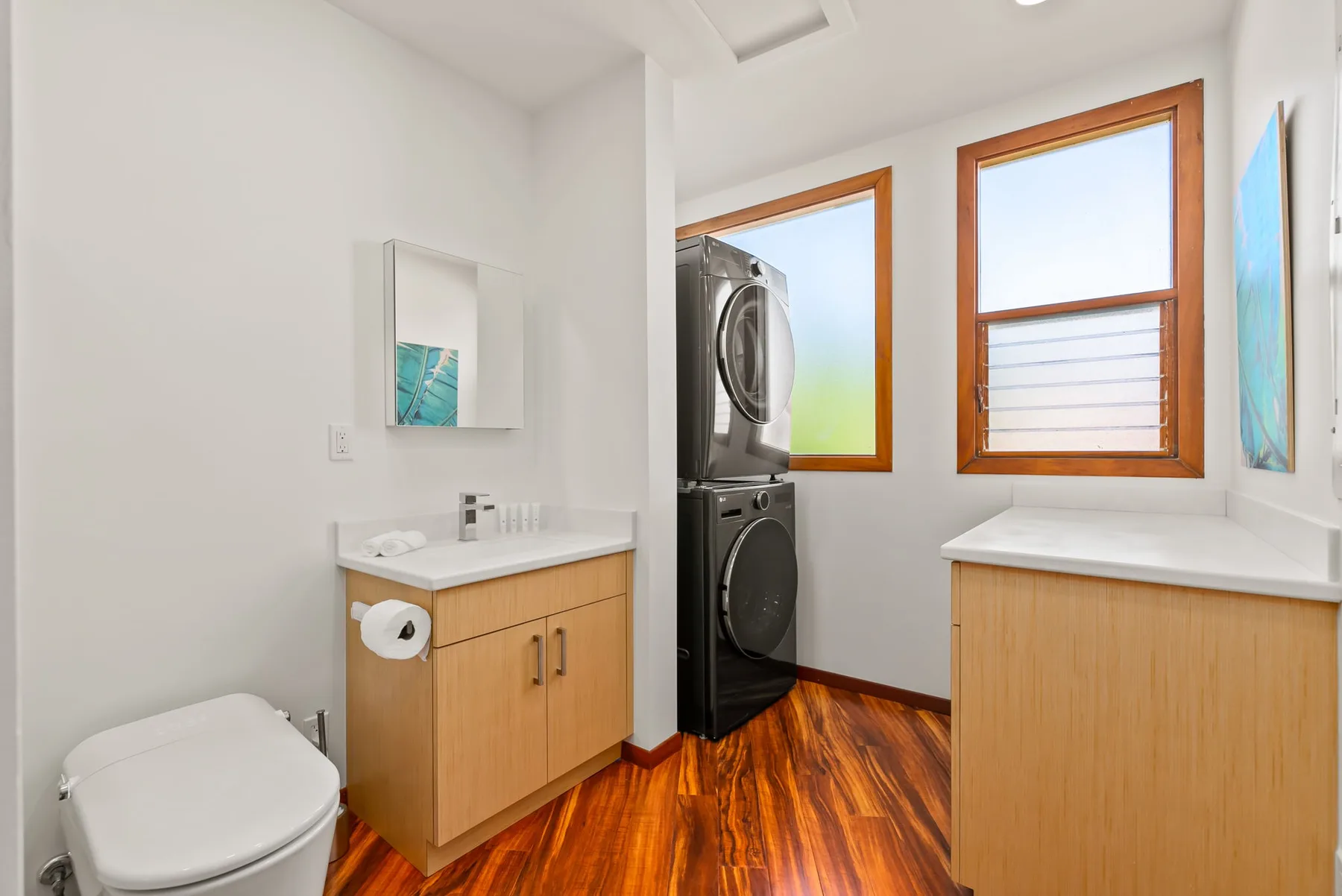 A bright laundry room with a stacked washer and dryer and wood cabinetry.