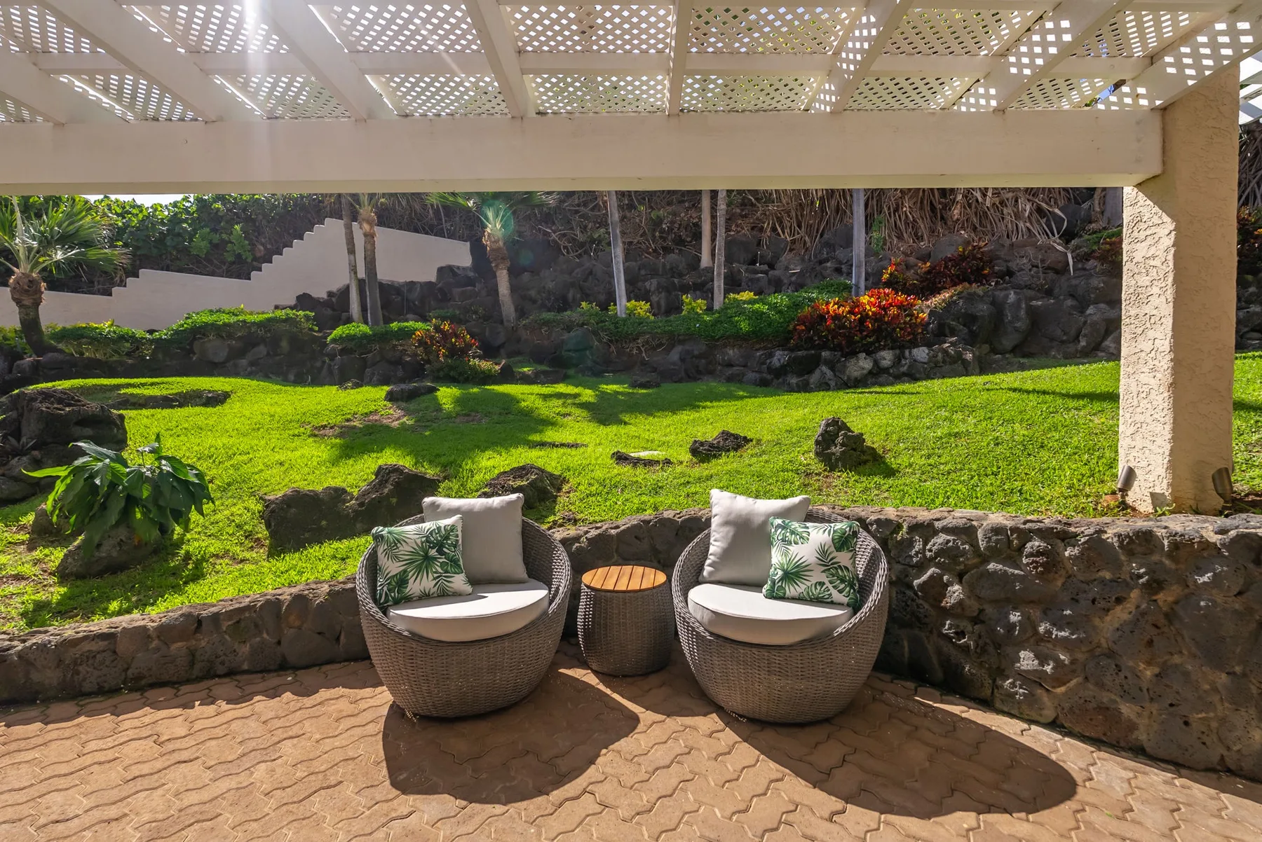 A garden patio with two cushioned seats beneath a pergola.