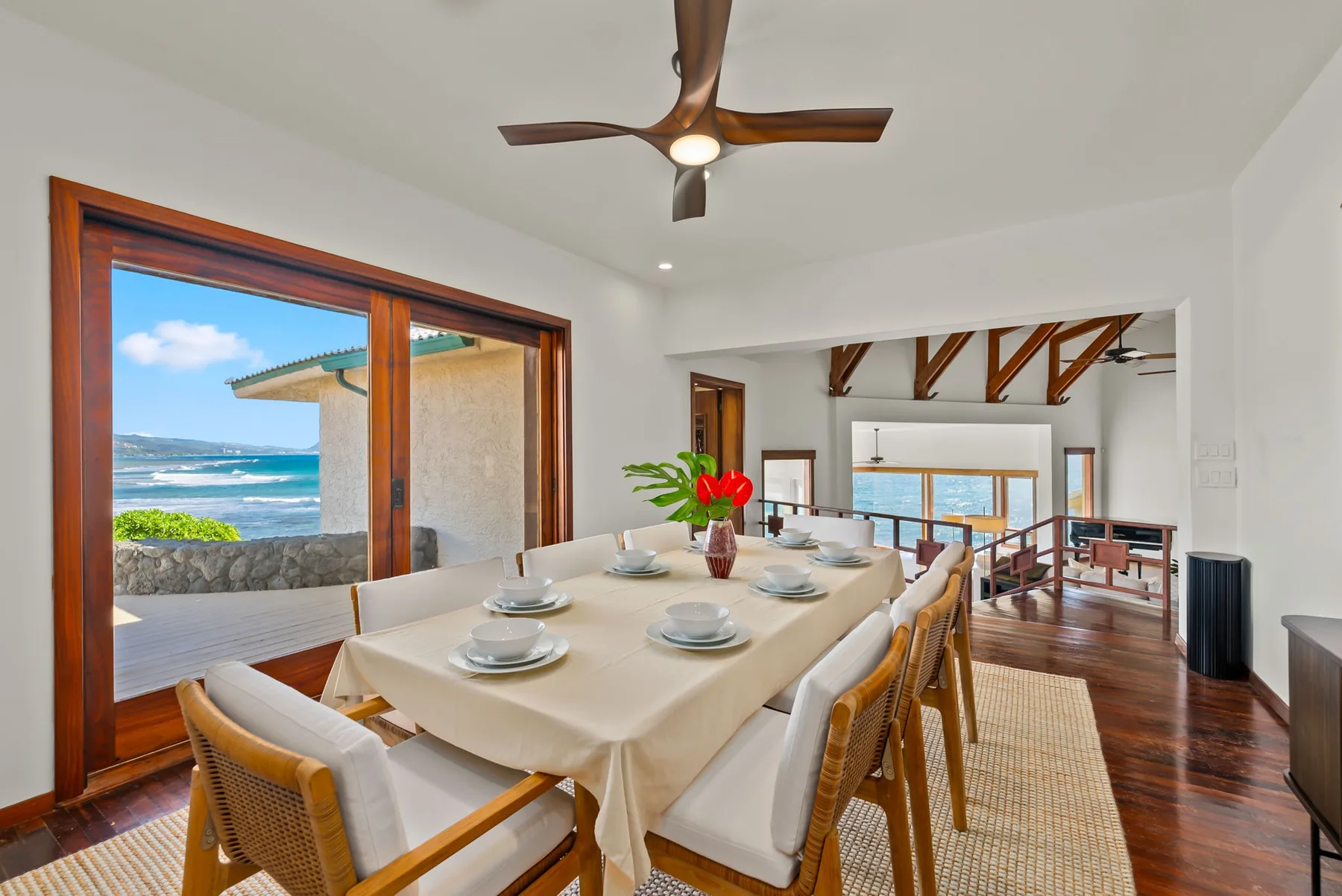 A bright dining area with a long table beside large windows overlooking the ocean.