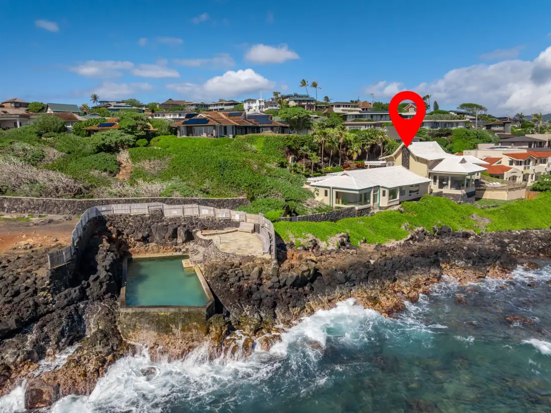 Aerial coastal view of homes above rocky shoreline and a small ocean pool.