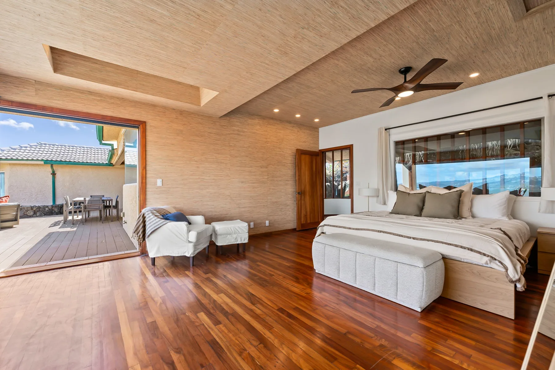 A bedroom with a large bed, seating area, and open doors to a patio.