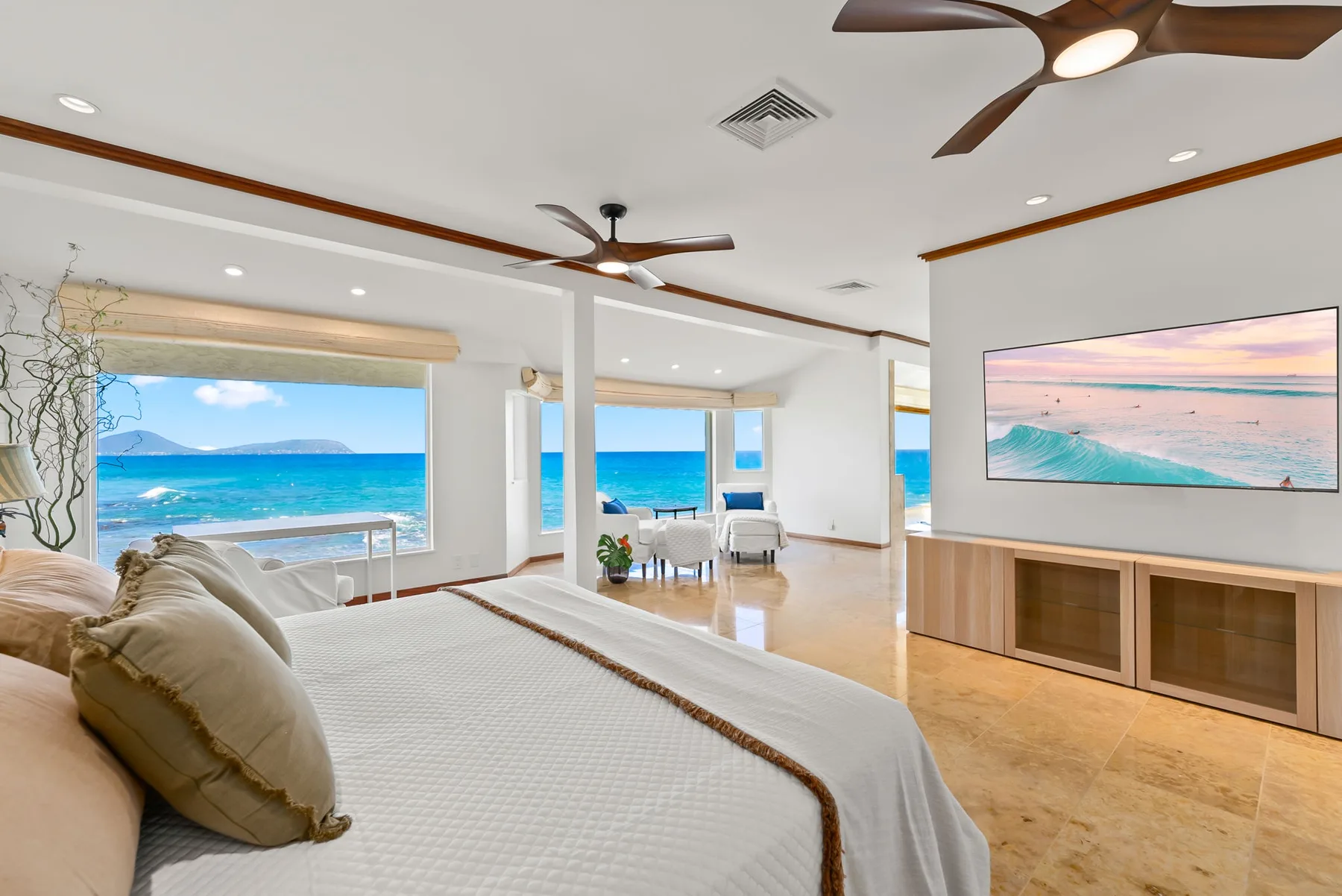 A bright bedroom with a bed, ocean views, and a seating area.