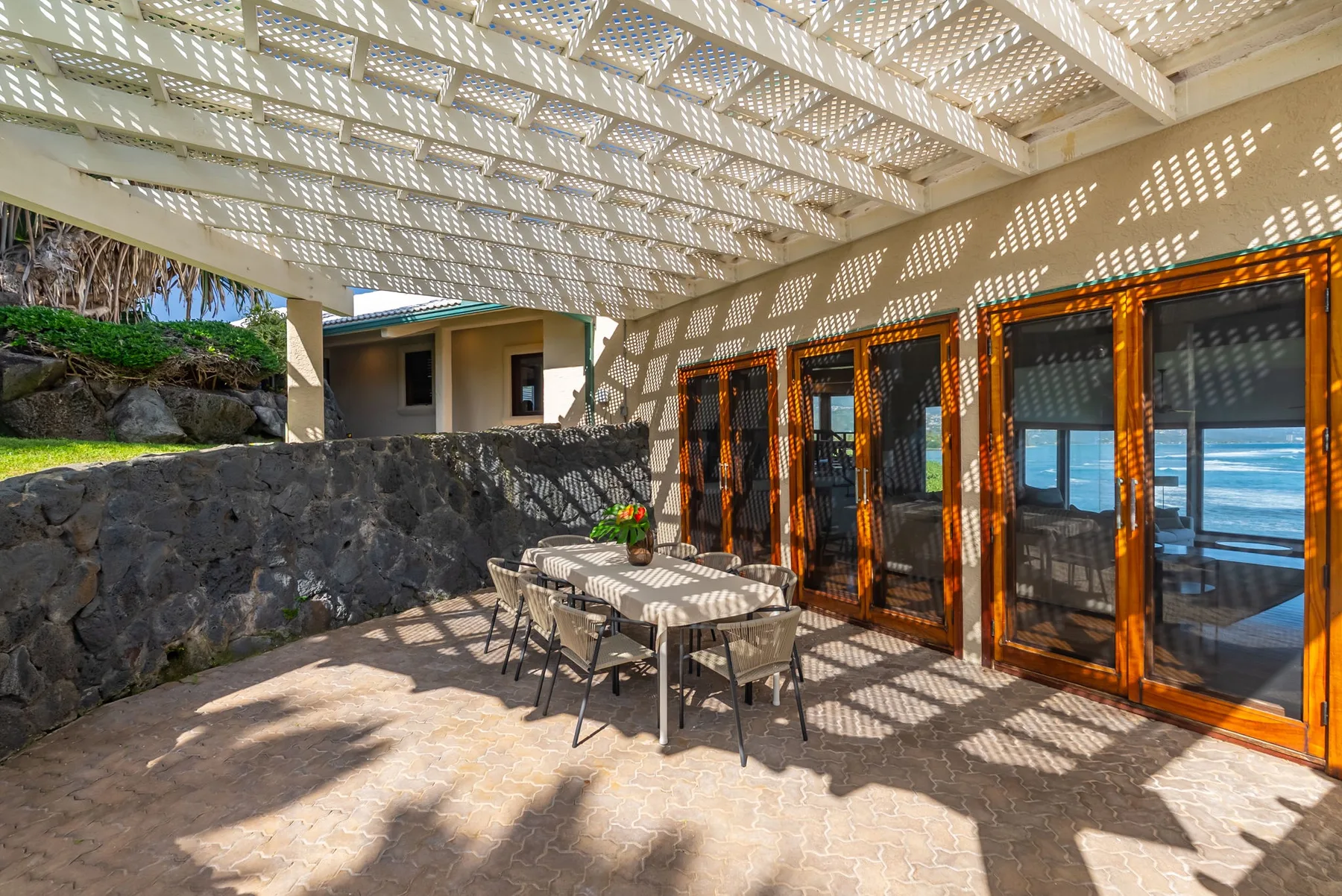 A covered outdoor dining area with a table and seating beside glass doors.