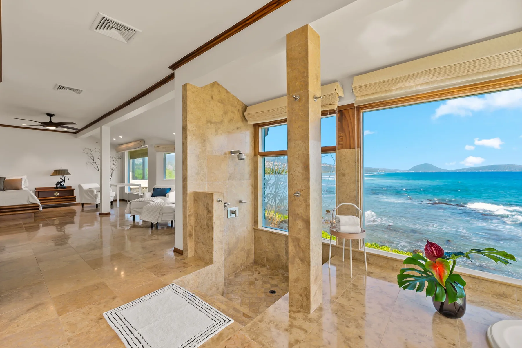 A bright seaside room with large windows overlooking the ocean and a potted plant.