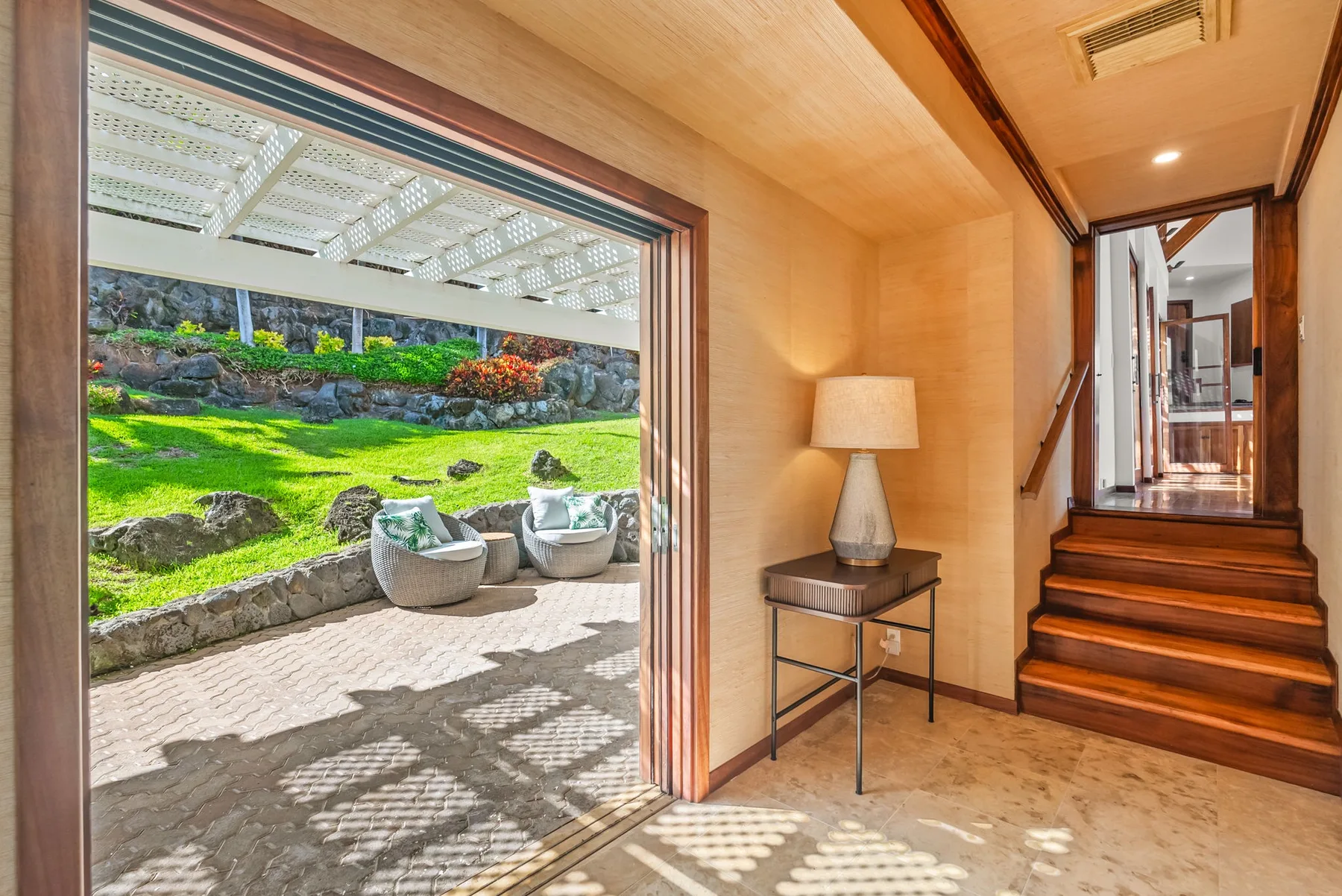 A warm-toned entryway opens onto a garden patio, with stairs leading to a hallway.