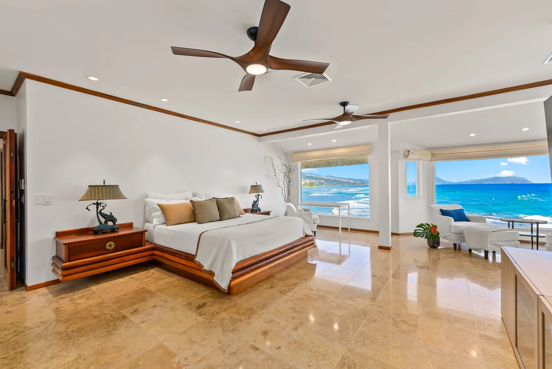 A bright bedroom opens onto a sitting area with large windows overlooking the ocean.