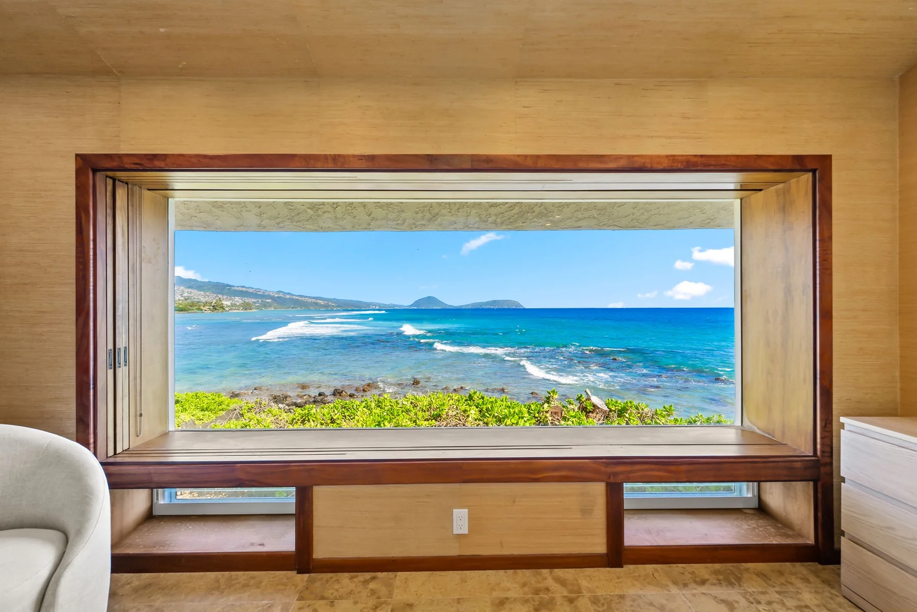A seaside room frames a blue ocean view through a wide wooden window.