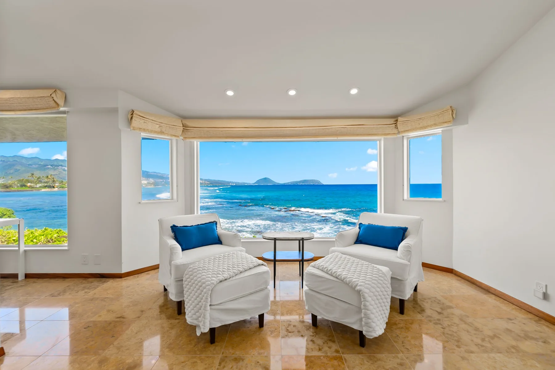 A bright living room with seating facing large windows overlooking the ocean.