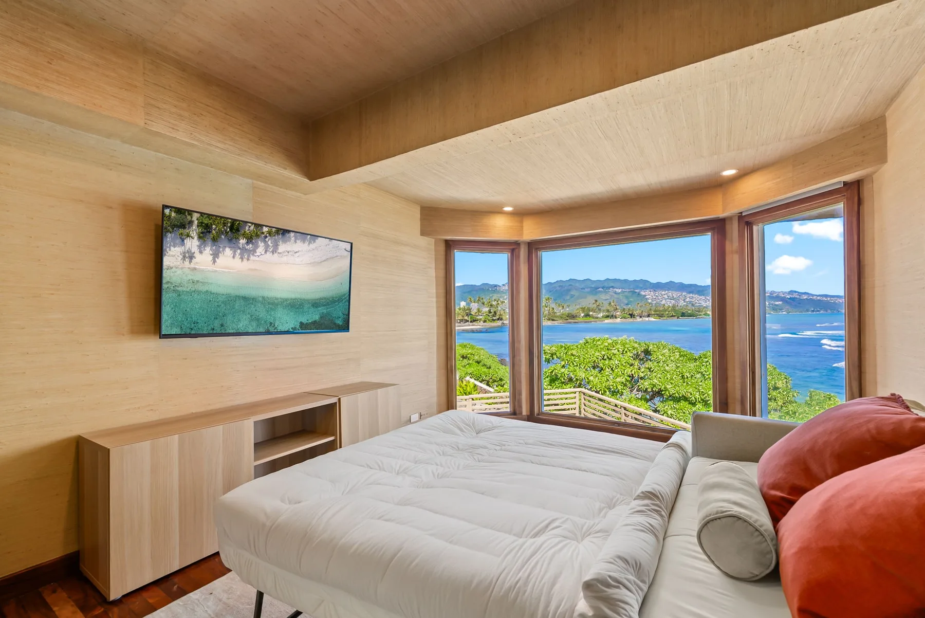 A bedroom with a bed beside large windows overlooking the water.