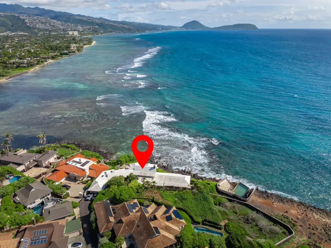 Aerial view of a coastal neighborhood beside a turquoise bay and breaking waves.