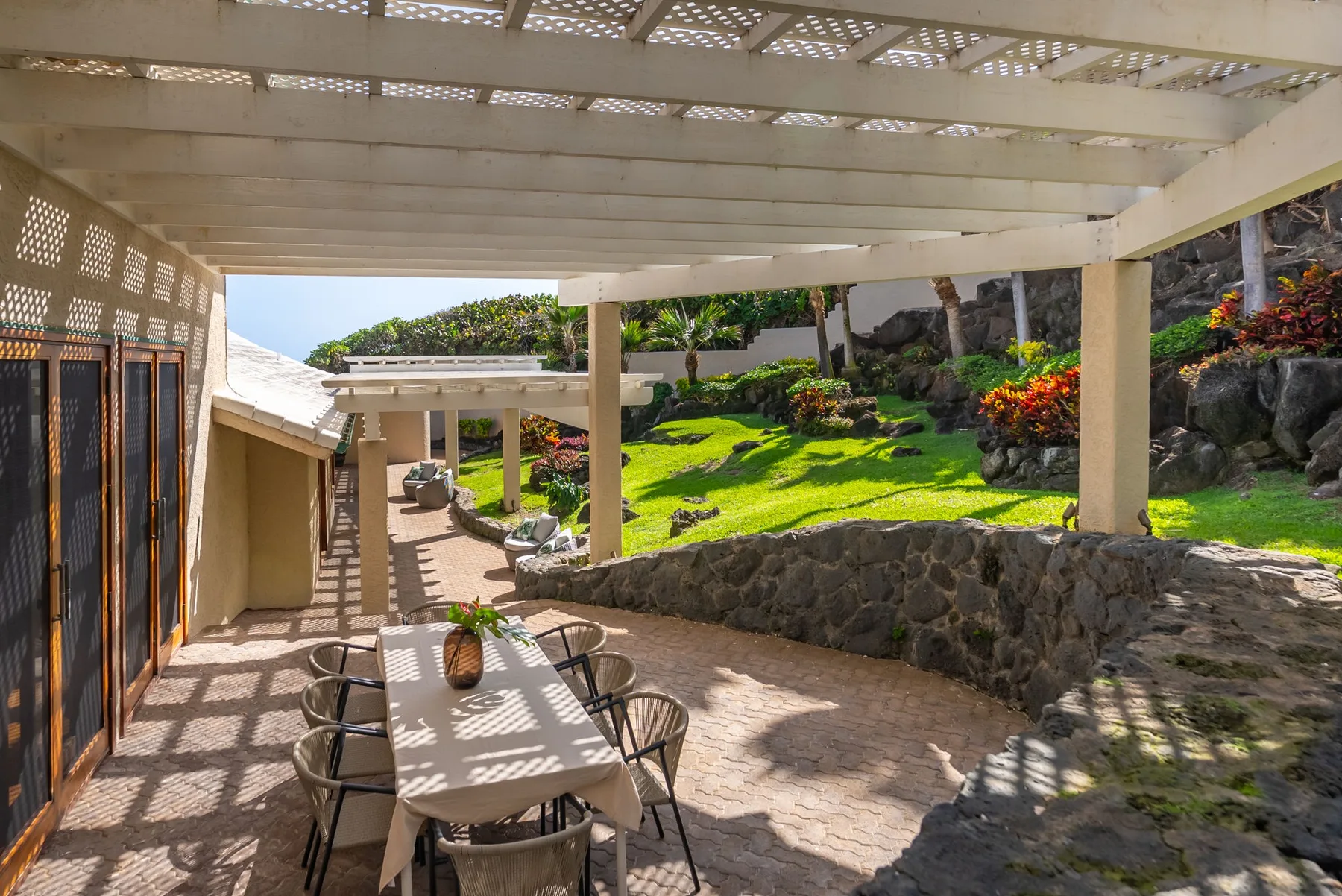 A covered outdoor patio with a dining table overlooks a landscaped garden.