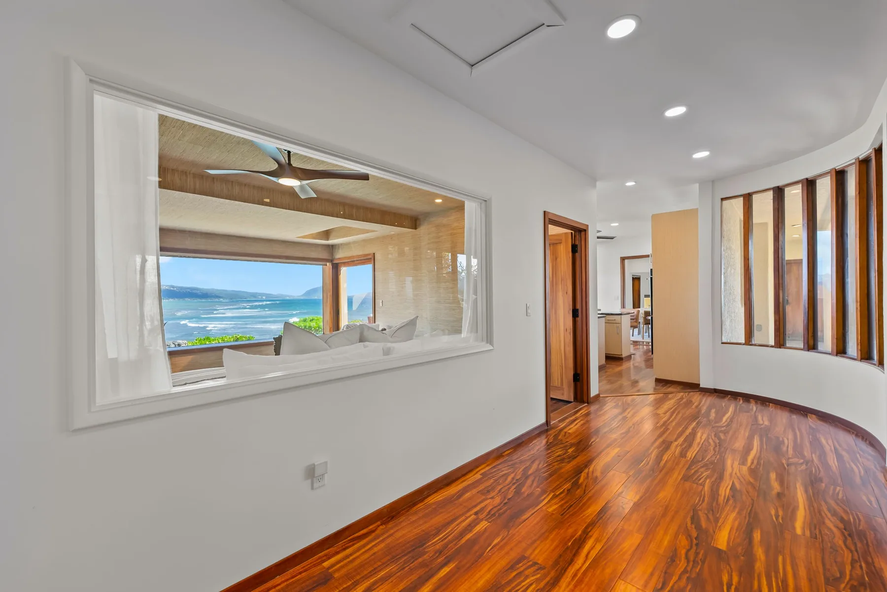 A bright interior hallway with polished wood flooring and a wide opening to a sitting area.