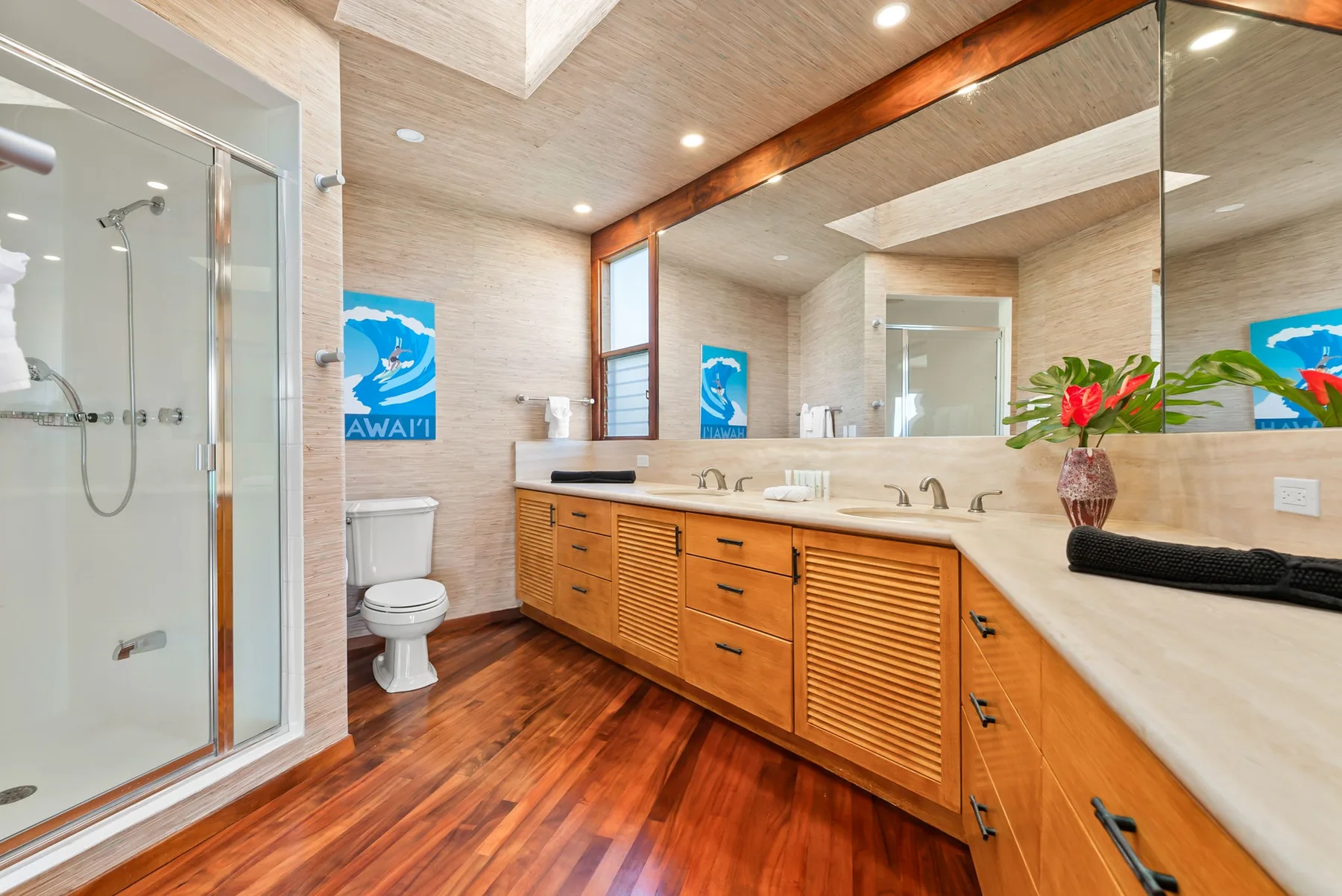 A bright bathroom with a glass shower, wooden vanity, and large mirror.