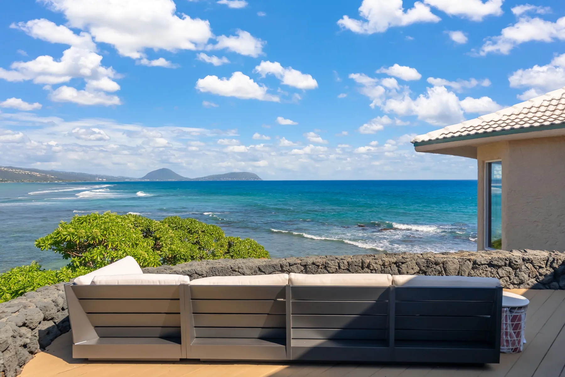 Oceanfront patio with outdoor seating overlooking the water and distant coastline.