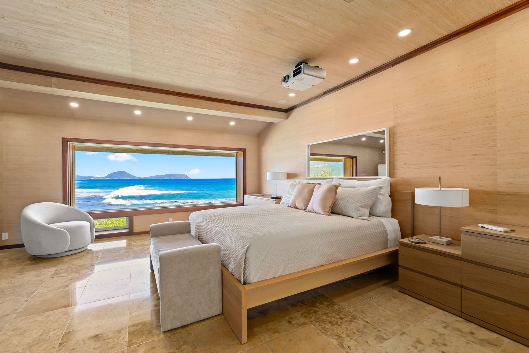 A bedroom with a large bed and a wide window overlooking the ocean.
