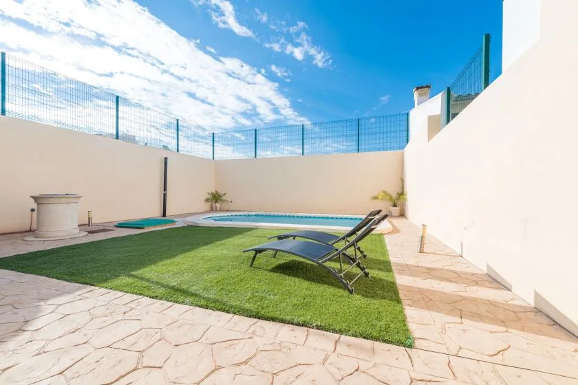 An outdoor patio with a small pool, lawn, and reclining loungers.