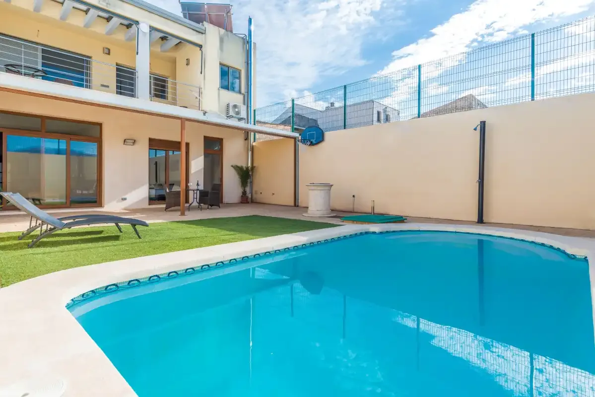 Una piscina al aire libre junto a un patio pavimentado y césped.