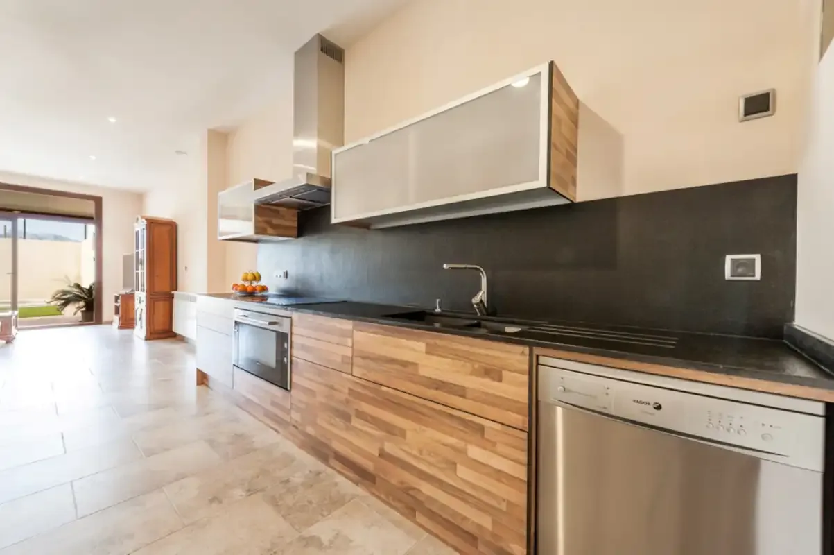 Una cocina moderna con muebles de madera, un salpicadero oscuro y electrodomésticos de acero inoxidable.
