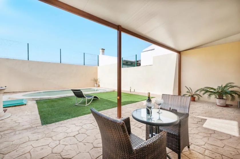 Un patio cubierto con asientos al aire libre da a un pequeño césped y una piscina.