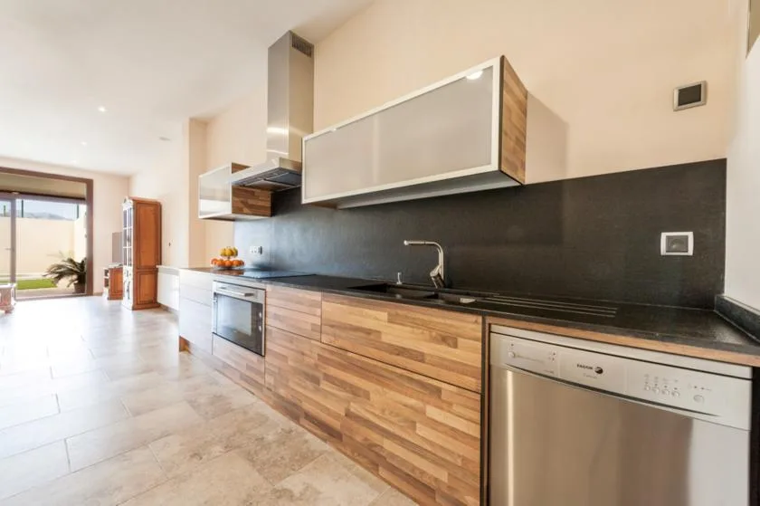 Una cocina moderna con gabinetes de acabado de madera, encimeras oscuras y electrodomésticos de acero inoxidable.