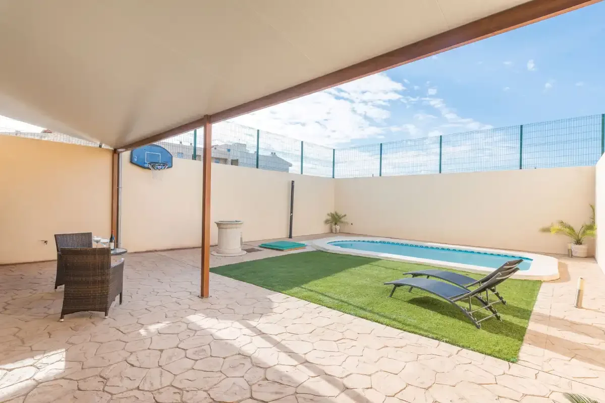 Un patio cubierto da a un césped y una piscina al aire libre.