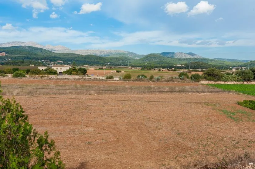 Un amplio paisaje rural muestra campos secos, edificios dispersos y colinas bajo un cielo nublado.