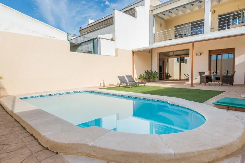 Una piscina en un patio está junto a una terraza con asientos al aire libre y puertas corredizas de vidrio.