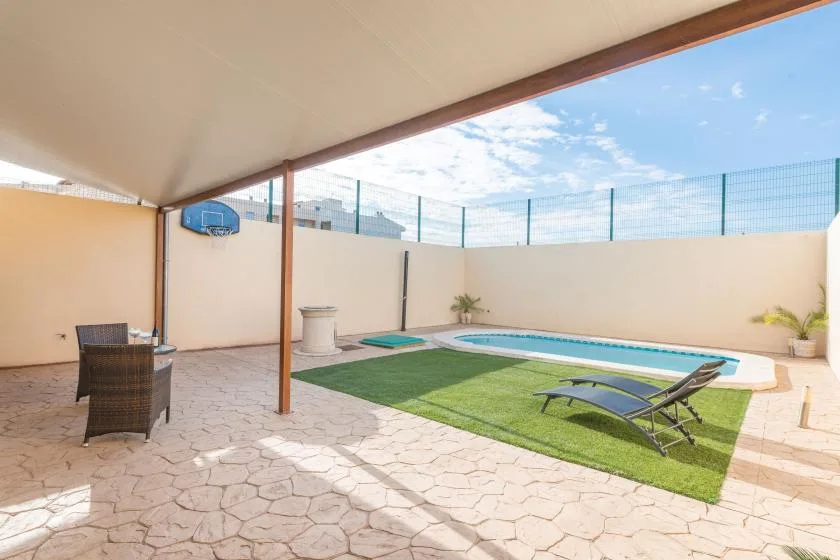 Un patio exterior cubierto da a una pequeña piscina y una zona de césped.