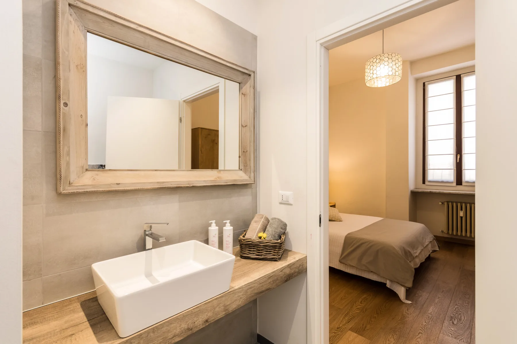 Un tocador de baño con lavabo y espejo da a un dormitorio.