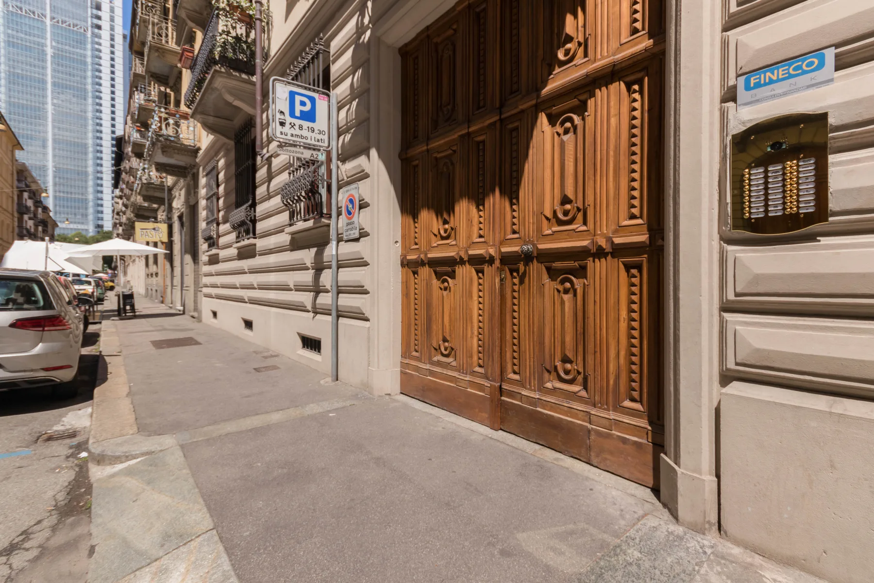 Una entrada de madera ornamentada está junto a una acera urbana y coches estacionados.
