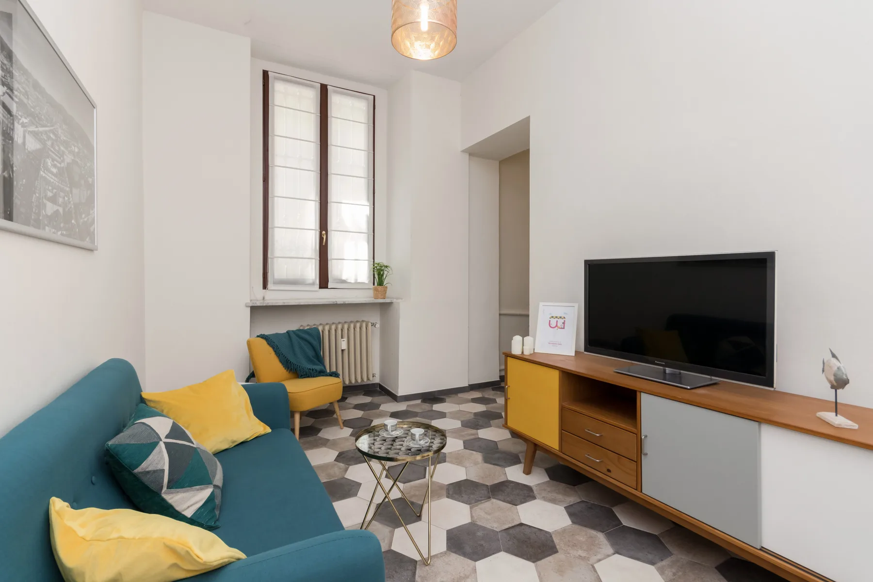 Una sala luminosa con asientos coloridos, un televisor y un suelo de baldosas estampadas.