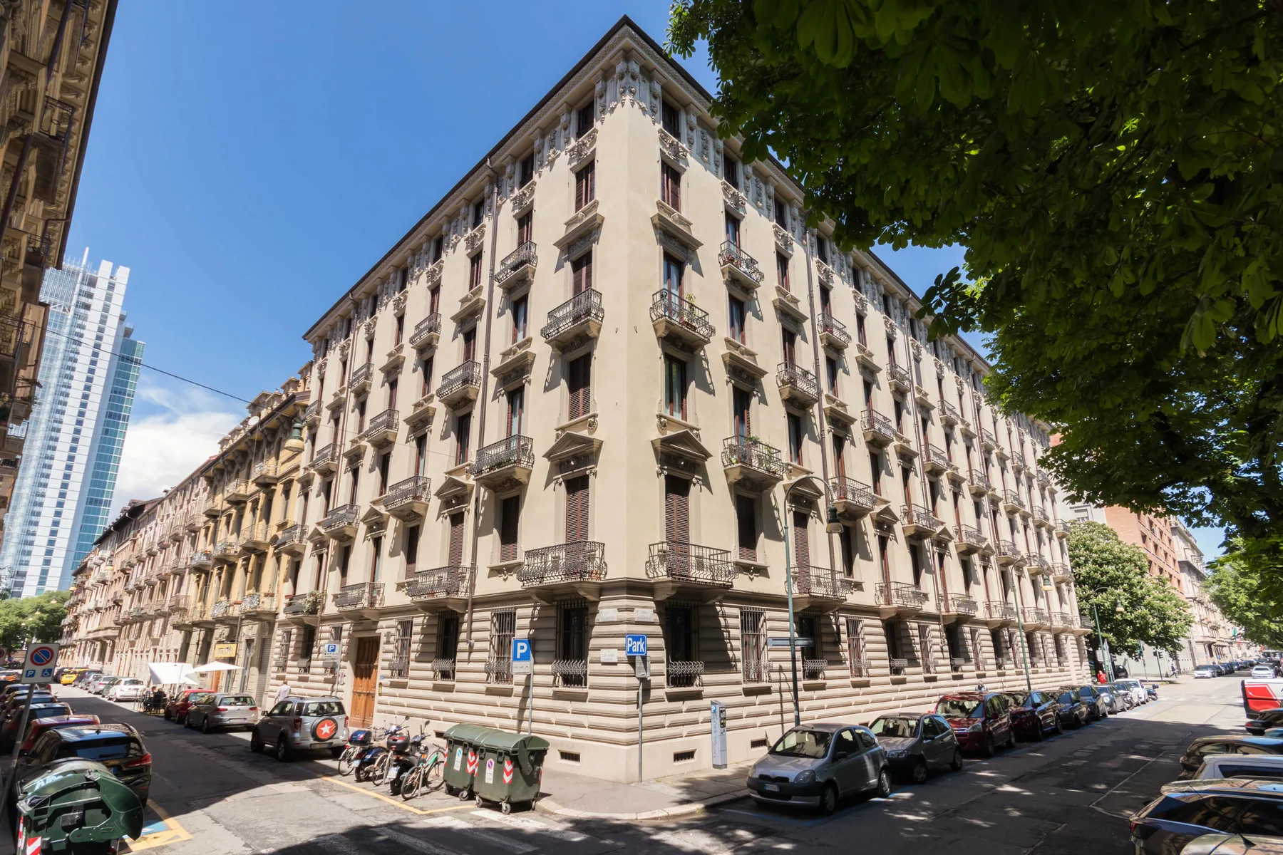 Un edificio esquinero de varios pisos con balcones ornamentados da a una calle urbana.