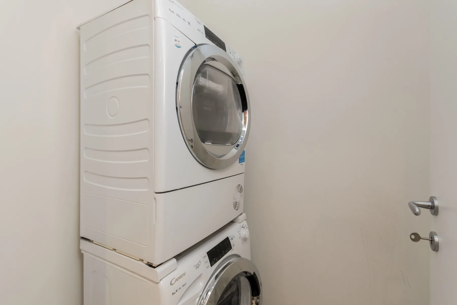 Una lavadora y secadora apiladas están junto a una puerta sencilla.