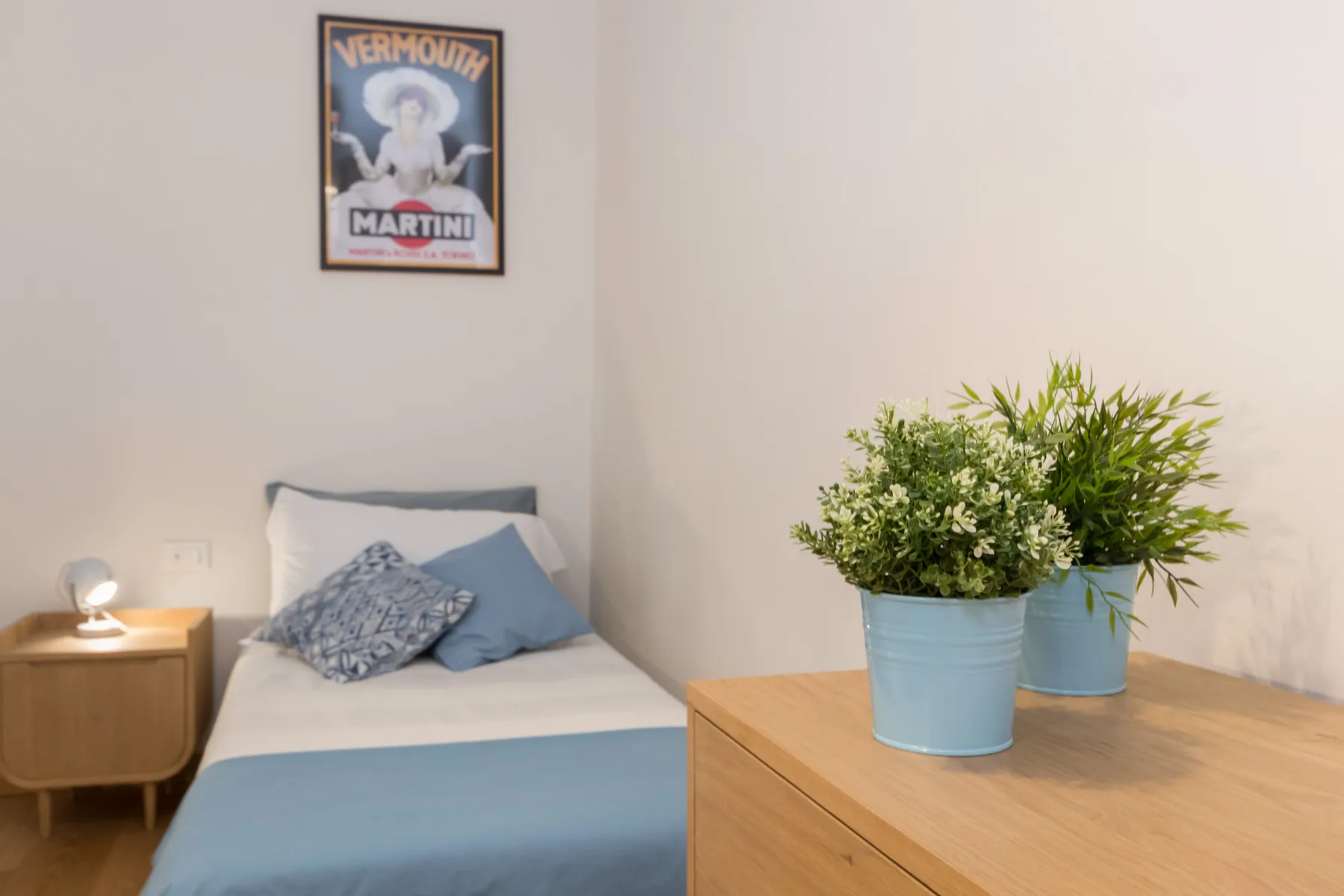 Un dormitorio con una cama tendida y plantas en macetas sobre una cómoda de madera.