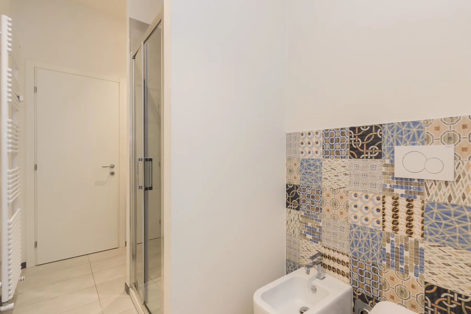 Un baño con un lavabo junto a una ducha de vidrio y azulejos estampados.