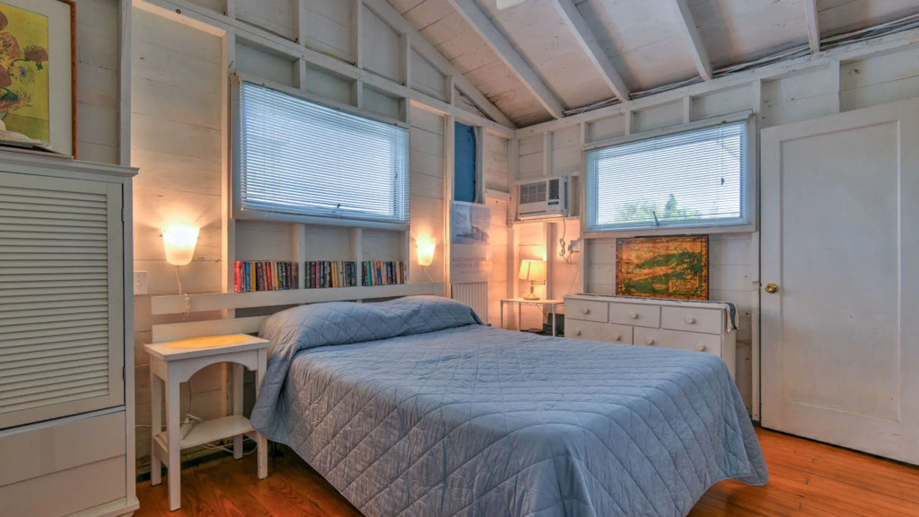 A bedroom with a bed, bedside tables, and windows along the walls.