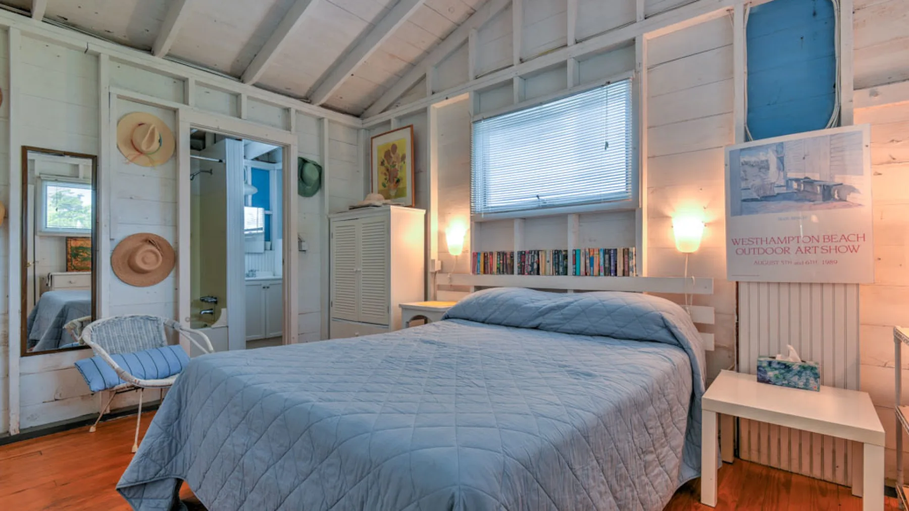 A bedroom with a bed beneath a window and books arranged along the wall.
