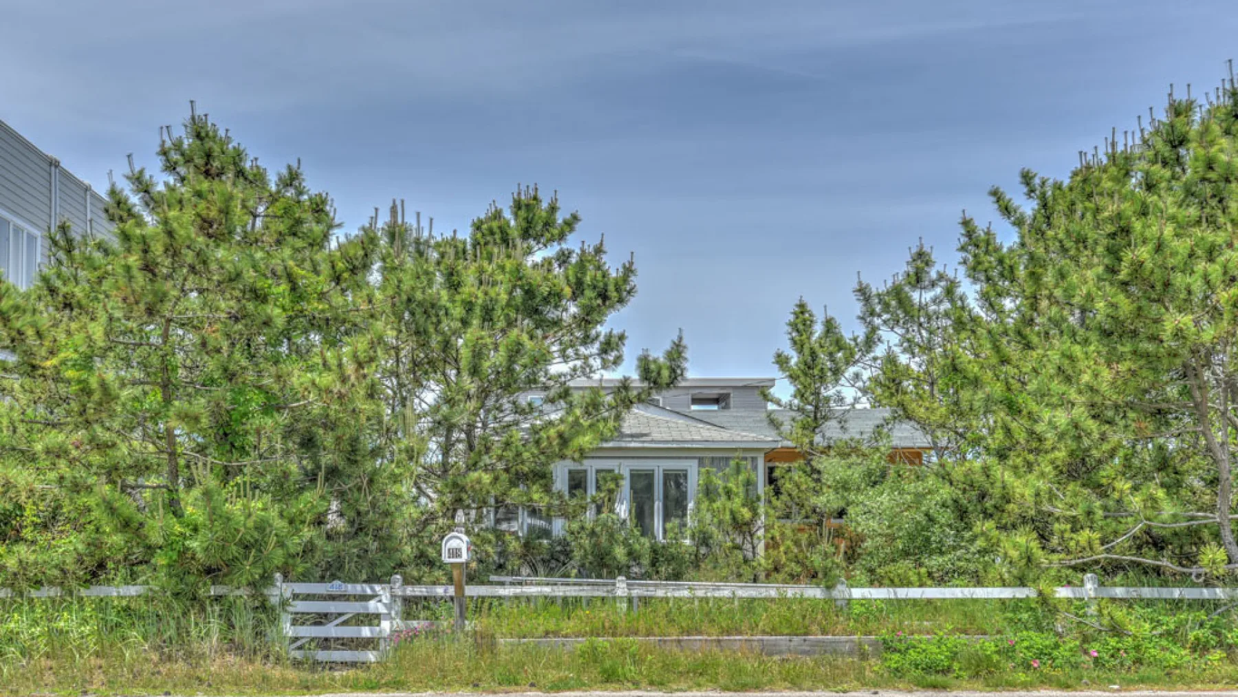 A house is partly visible behind trees and a low fence.
