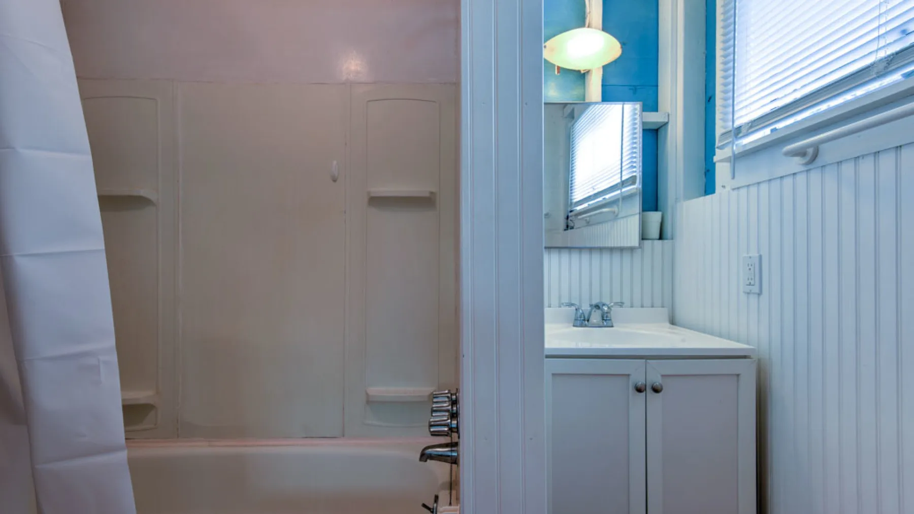 A bathroom with a bathtub, vanity, and window blinds.