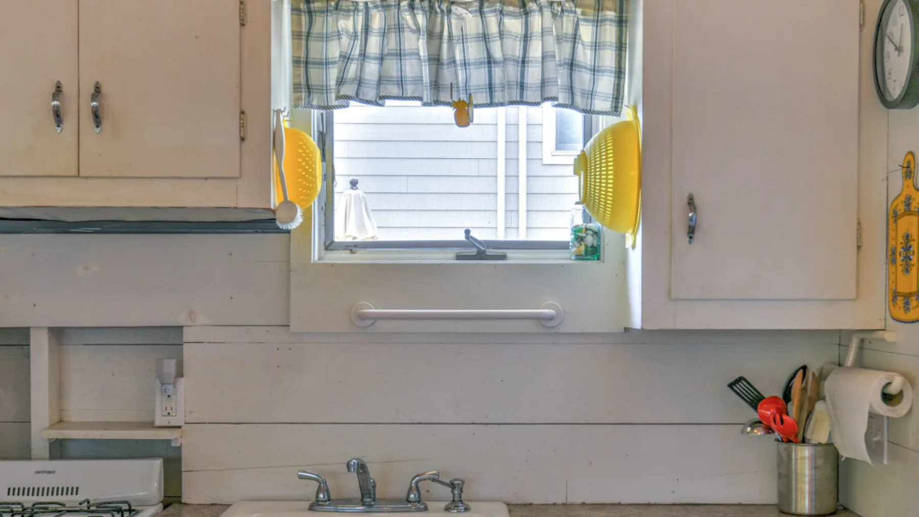 A kitchen sink sits beneath a window with a checked curtain.