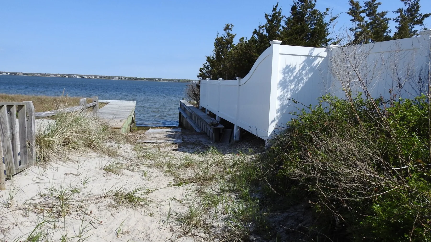 A sandy path leads through coastal vegetation to a waterfront.