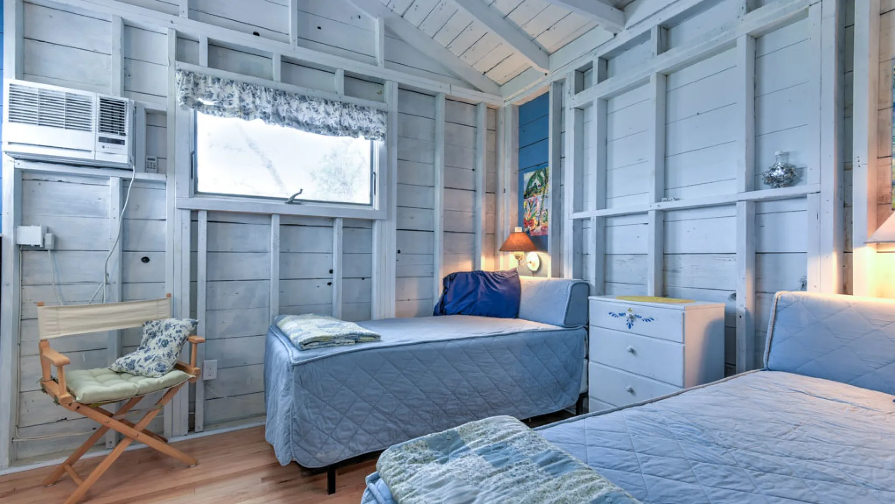 A bedroom with two beds, a dresser, and pale wood-paneled walls.